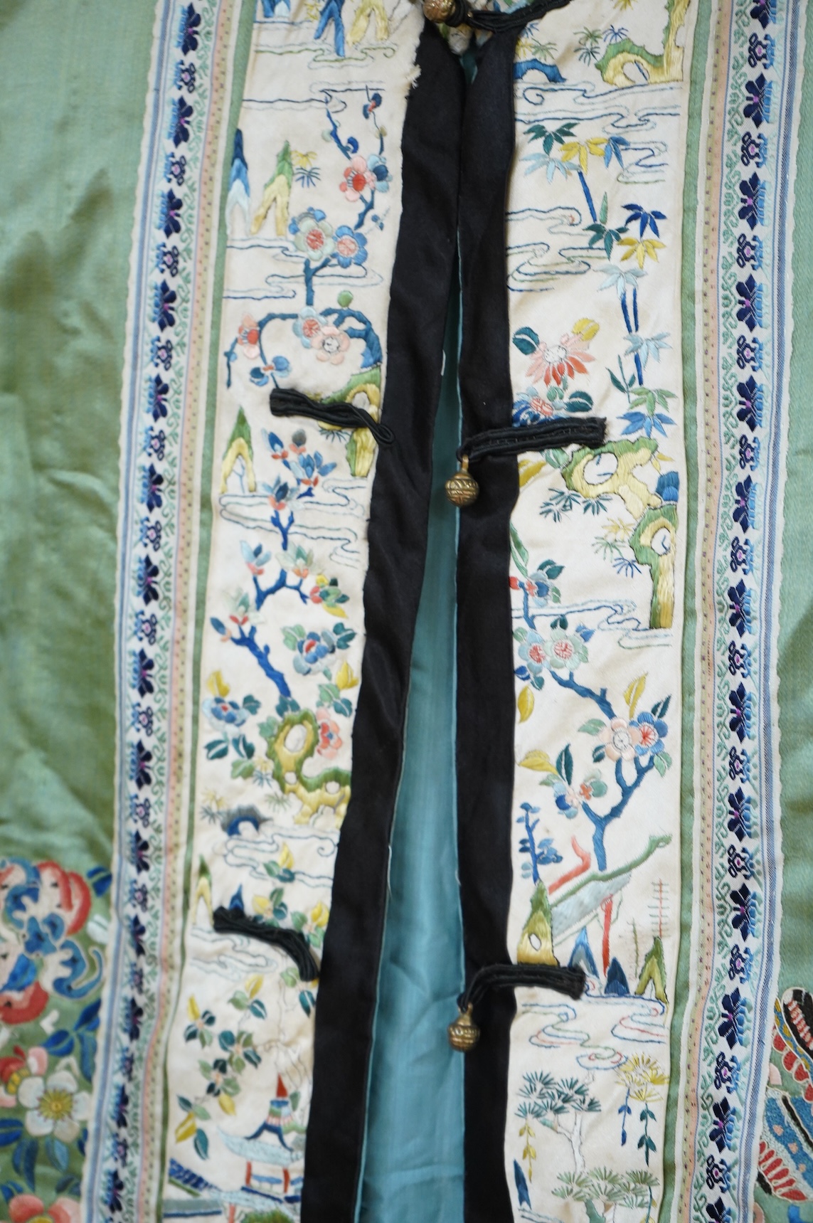An early 20th century Chinese green silk polychrome embroidered jacket. Worked with Chinese knot embroidery and stem stitch into flowers, butterflies and bats, edged with woven silk ribbon and a figurative embroidered bo